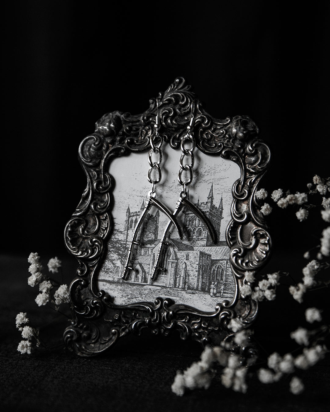 Vista de los Scythe Earrings de The Pretty Cult con diseño de guadaña plateada